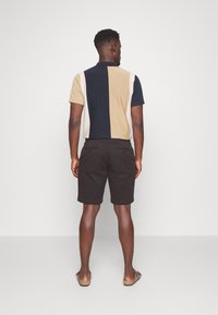 Polohemd met korte mouwen in een kleurblokontwerp in marineblauw, beige en crèmekleur, gecombineerd met donkerbruine shorts, weergegeven vanuit de achterkant.