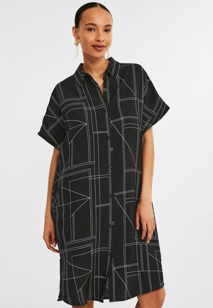 Zwarte shirtjurk met korte mouwen, met een geometrisch patroon van witte lijnen. Gemaakt van zachte stof, heeft het een relaxte, losse pasvorm.