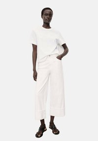 White cotton t-shirt and wide-leg white trousers with a hem detail, paired with black sandals. The outfit has a casual, minimalist design.