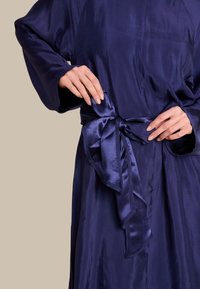 Marineblå satinbadekåpe med knytbelte, lange ermer og en glatt tekstur med lett glans. Detaljene inkluderer en subtil glans og pent ferdige kanter.