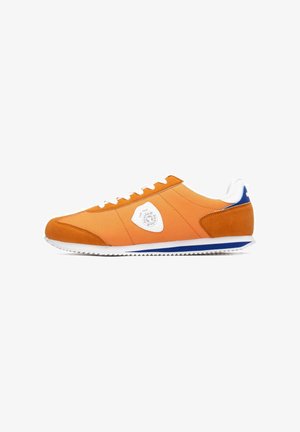 Zapatilla de tela y ante naranja con cordones blancos, un parche con el logo blanco en el costado y un detalle azul en el talón. Suela de goma con tracción.
