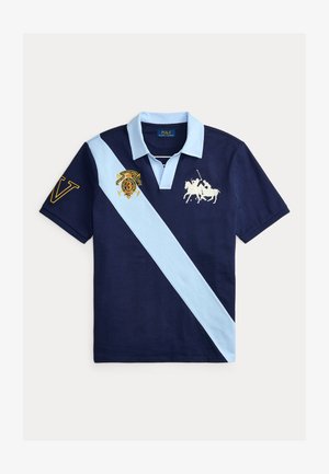 Granatowa koszulka polo z jasnoniebieskim ukośnym paskiem. Na piersi haftowany biały koń z jeźdźcem oraz złote logo, na rękawie litera "V".