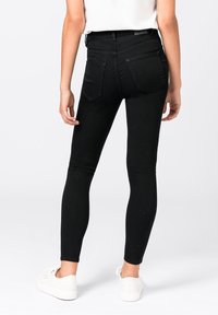 Jeans negros ajustados con un diseño entallado, hechos de denim, con bolsillos traseros y una cintura de altura media, combinados con zapatillas blancas.