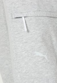 Grijze joggers met een zachte textuur, voorzien van een voorvak met een witte rits en een wit Puma-logo aan de zijkant.