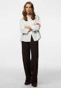 Bijela košulja s dugmadima i podvrnutim rukavima, uparena s tamnocrnim hlačama širokih nogavica. Jednostavan dizajn s opuštenim krojem i čistim linijama.