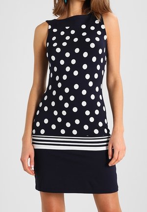 Ärmelloses marineblaues Kleid mit großen weißen Punkten oben, horizontalen weißen und marineblauen Streifen an der Taille und einfarbigem marineblauen Rock.