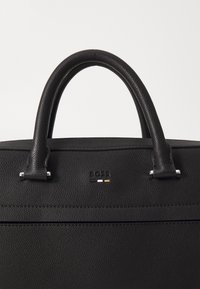 Sac à main en cuir noir avec une surface texturée, deux poignées et un petit logo en accent. Equipé de quincaillerie en argent et d'un design épuré et minimaliste.