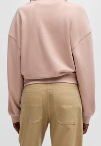 Różowa, zakurzona bluza z okrągłym dekoltem i prążkowanym wykończeniem na dole, zestawiona z beżowymi spodniami z dwoma tylnymi kieszeniami i detalami przeszyć.