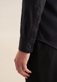 Camicia nera in tessuto texturizzato con polsini abbottonati, caratterizzata da un motivo sottile e un tessuto liscio, completata da una vestibilità su misura e linee pulite.