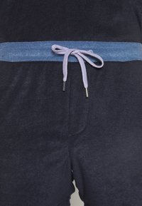 Gros plan d'un short bleu marine avec une ceinture bleu clair et un cordon lavande noué avec des embouts métalliques.