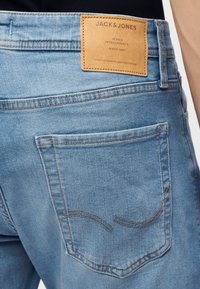 Ανοιχτό μπλε τζιν με πίσω τσέπη και μια ταμπέλα από ταμπά δέρμα με την επιγραφή "Jack & Jones" ραμμένη στη ζώνη μέσης.