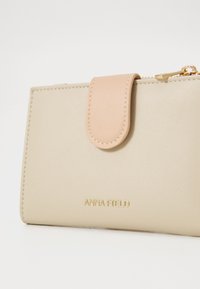 Beige lommebok laget av glatt lær, med en lys rosa klaff og gullmerke. Glidelåsdetalj øverst for sikker lukking.