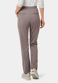 Grijze, aansluitende joggers met een elastische tailleband, twee achterzakken en een gladde textuur, gecombineerd met lichtgekleurde sneakers met gouden accenten.