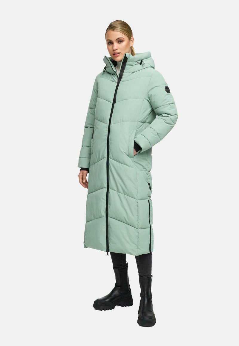Woman wearing a long, quilted light green puffer coat with a hood, black zipper, side zippers, black pants, and chunky black boots.