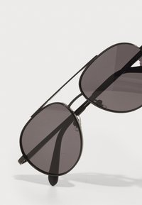 Ochelari de soare negri cu lentile supradimensionate, rotunde. Cadru subțire din metal cu un design minimalist. Lentile gri închis oferă protecție împotriva soarelui.