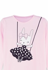 Rosa Hemd mit einem weißen Hasen, der ein gepunktetes Kleid und eine Schleife trägt, lächelt mit geschlossenen Augen auf einer Schaukel.