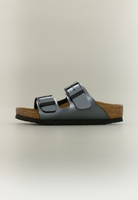 Επίπεδη σανδάλι με δύο ρυθμιζόμενους γκρι δερμάτινους ιμάντες, πάτο από φελλό και μαύρη λαστιχένια σόλα, εμφανιζόμενο σε πλαϊνή όψη σε ουδέτερο φόντο.