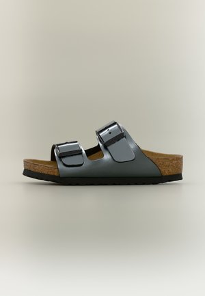 Lygus sandalai su dviem reguliuojamomis pilkomis odinėmis juostelėmis, kamštine padu ir juodu guminiu padu, parodyti šoniniu profiliu ant neutralaus fono.