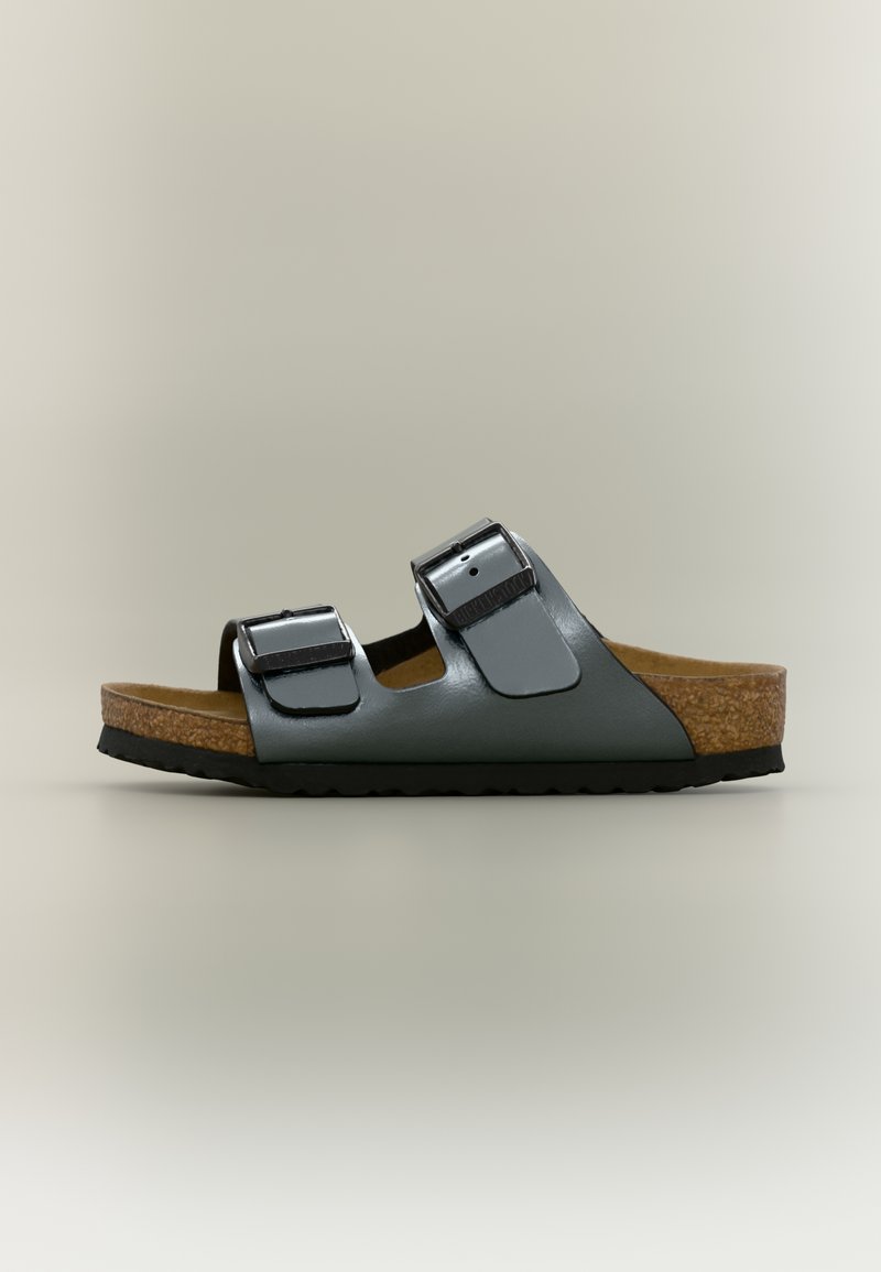 Επίπεδη σανδάλι με δύο ρυθμιζόμενους γκρι δερμάτινους ιμάντες, πάτο από φελλό και μαύρη λαστιχένια σόλα, εμφανιζόμενο σε πλαϊνή όψη σε ουδέτερο φόντο.