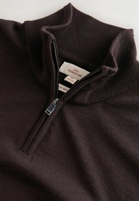 Ciemnobrązowy sweter z wełny merino z zamkiem błyskawicznym o długości ćwierć, z wysokim kołnierzem i srebrnym zamkiem, pokazujący wewnętrzną metkę z informacjami o marce i rozmiarze.