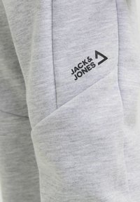 Szare dresy wykonane z miękkiego materiału, z charakterystycznym ukośnym wzorem kieszeni i czarnym logo "JACK & JONES" nadrukowanym na udzie.