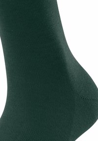 Dunkelgrüner, nahtloser Sockenstoff im Close-up, der die Strickstruktur rund um den Knöchel- und Fersenbereich hervorhebt.