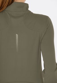 Olivgrüne Sportjacke mit hohem Kragen, aus strukturiertem Stoff und reflektierenden vertikalen Linien auf der Rückseite.