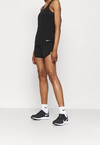 Musta hihaton paita ja shortsit, joissa on Nike-logo, yhdessä mustien urheilujalkineiden ja valkoisten sukkien kanssa. Yksinkertainen, urheilullinen muotoilu ja vartaloa myötäilevä istuvuus.