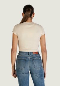 Crop top à manches courtes de couleur crème avec une texture côtelée, associé à un jean en denim bleu taille haute avec poches arrière et étiquette de marque.