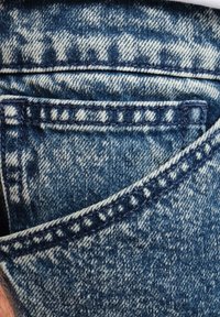 Tela de mezclilla azul que muestra un primer plano de un bolsillo con costuras en contraste y textura desgastada, presentando un diseño clásico de cinco bolsillos.