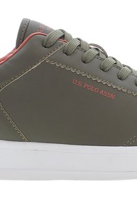 Sneaker in pelle verde oliva con suola in gomma bianca, lacci abbinati e dettagli rossi. Presenta il marchio "U.S. POLO ASSN." sul lato.