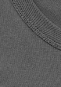 Grauer Baumwollstoff mit glatter Textur, ausgestattet mit einem gerippten Rundhalsausschnitt und gleichmäßigen, konsistenten Nähten.