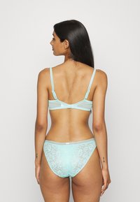 Conjunto de lingerie azul claro em renda, apresentando um sutiã transparente com alças ajustáveis e uma calcinha de cintura alta combinando com padrões florais.