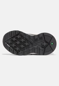 Černá gumová podrážka obuvi se strukturovaným grip vzorem, obsahující hexagonální a křížové profily pro trakci. Výrazný centrální zelený akcent.