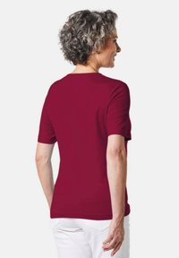 Bordeaux kortekorte mouwen t-shirt met een ronde halslijn, zachte stof, een getailleerd ontwerp en subtiele schoudernaden, gedragen met witte broeken.