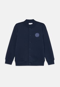 Veste sweat bleu marine avec col rond, boutons pression sur le devant, poignets côtelés et détail de logo circulaire sur la poitrine gauche.