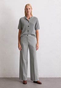 Top corto a maniche corte grigio a coste con bottoni abbinato a pantaloni larghi grigio chiaro. Scarpe con tacco marroni completano l'outfit.