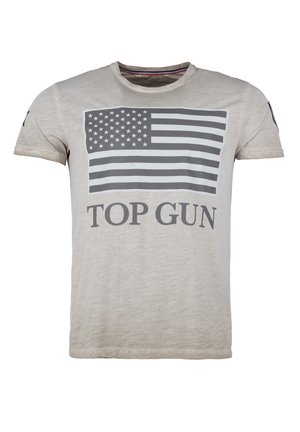 Jasno-beżowa koszulka z bawełny, z szarym nadrukiem amerykańskiej flagi i napisem "TOP GUN" poniżej. Krótkie rękawy, okrągły dekolt.