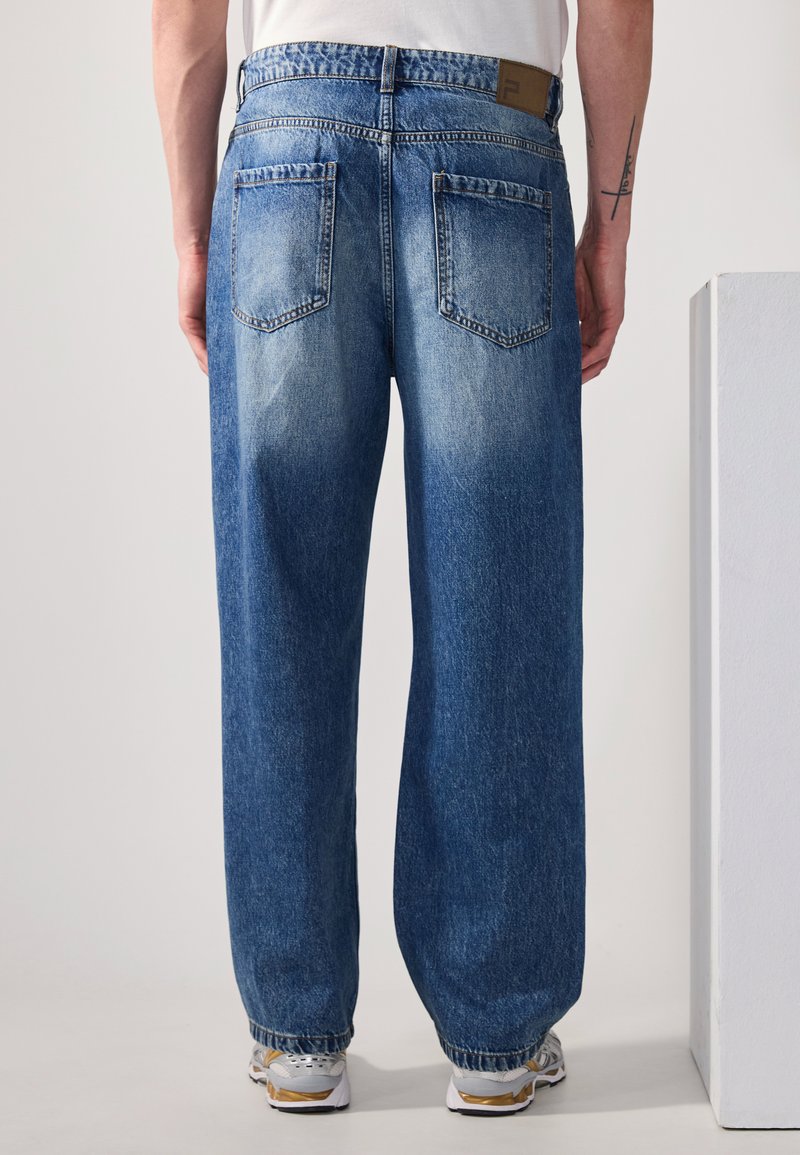 Jeans in denim blu sbiadito a gamba larga, con una texture lavata, design a cinque tasche e polsini elasticizzati. La parte posteriore presenta l'etichetta del marchio e dettagli delle cuciture.