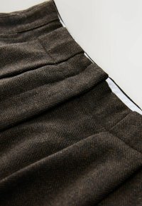 Wollrock mit einem Fischgrätenmuster in Brauntönen, ausgestattet mit Falten und einem kontrastierenden weißen Futter entlang der Taille.