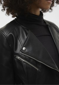 Zwarte leren motorjas met een asymmetrische ritssluiting, zilverkleurige hardware en gestructureerde schouderdetails. Soepele en aangesloten pasvorm.