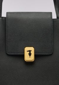 Svart läderhandväska med en texturerad yta, rektangulär form, klaffstängning och ett guldspänne med ett präglat mönster.