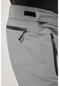 Pantaloni da escursionismo grigi con una texture di tessuto liscia, chiusura in velcro e tasche con zip con accenti neri a contrasto.