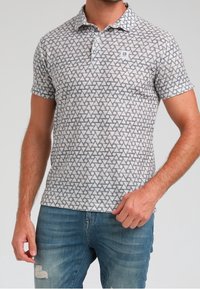 Kortärmad polo i ljusgrått med ett triangulärt mönster. Har tre knappar och en liten logotypklistermärke. Tillverkad av en blandning av bomull.