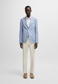 Ljusblå linnジャacket med flikiga kragar, vit skjorta, krämfärgade byxor och tan skor. Innehåller en ficknäsduk och lapelaccessoar.