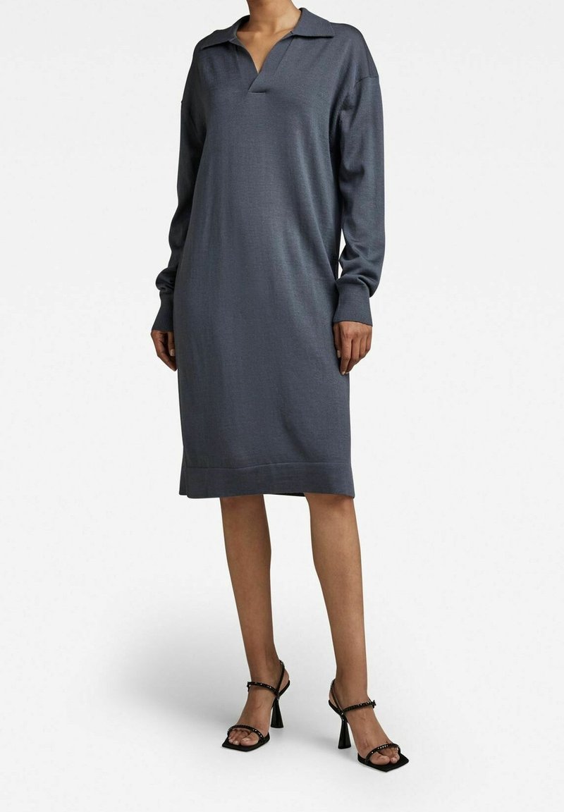 Långärmad, kragad klänning i mörkgrått stickat material, med en avslappnad passform och ribbad nederkant. Bärs med svarta remsandaler med klack.