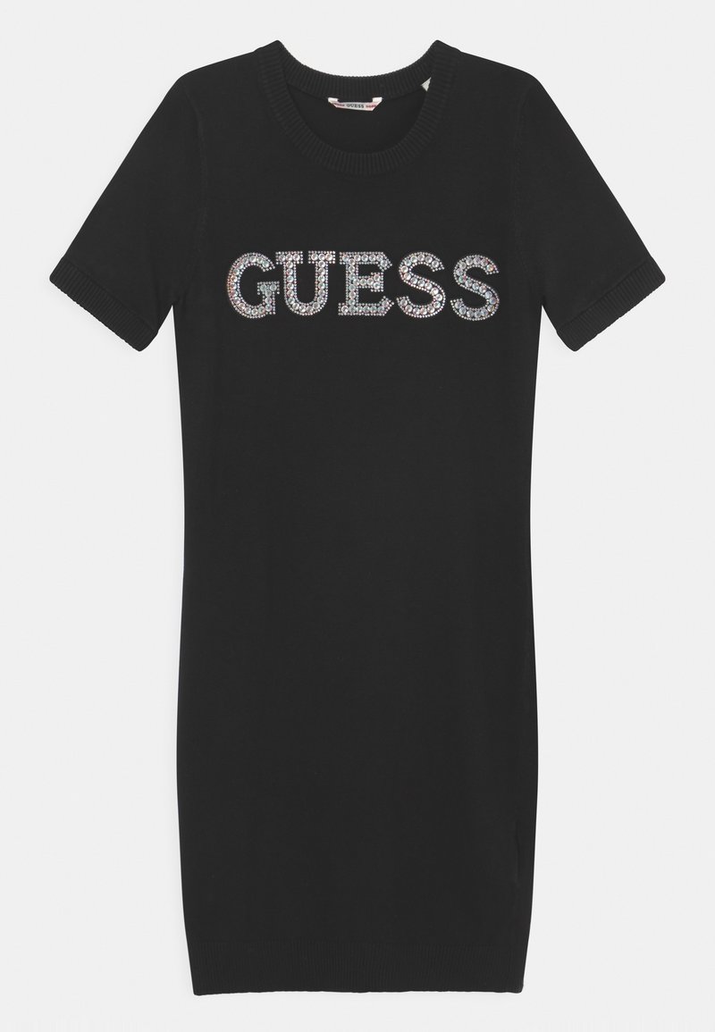 Robe en maille noire à manches courtes avec col et manches côtelés, arborant le mot « GUESS » en grandes lettres de strass scintillants sur la poitrine.