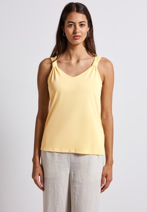 Haut sans manches jaune avec un col en V, présentant des accents froncés sur les bretelles et une texture douce et lisse. Suggestion d'association avec un pantalon en lin clair.