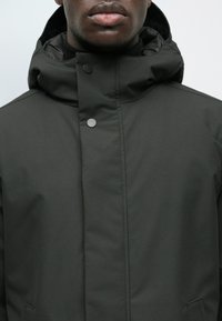 Giacca nera impermeabile con un alto colletto, chiusure a scatto e una texture liscia, progettata per il clima freddo.