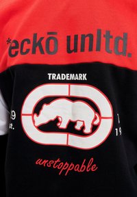 Kortsleeve t-skjorte med røde og svarte fargeblokker, en stor grafikk med en nesehornsilhuett, og teksten "eckō unlt." og "ustoppelig."